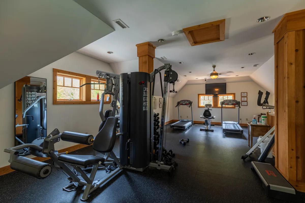 A modern, well-lit fitness room with multi-gym equipment and several treadmills positioned in front of large windows that offer mountain views. The mood is energetic and motivating, ideal for guests looking to keep up with their fitness routines while on vacation.