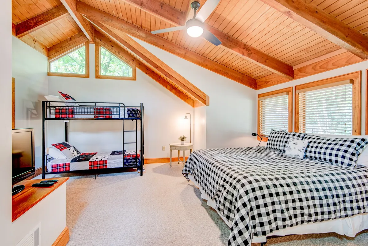 A spacious bedroom with both a large bed and a bunk bed, accented by exposed wooden beams and generous windows. The room offers flexible sleeping options ideal for families or groups, making it playful yet comfortable.