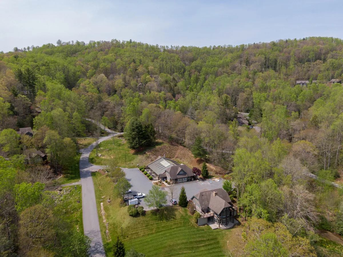 This image features the main building framed by tall, lush trees and a winding road, evoking an immediate sense of connection to nature and adventure. The tranquil mountain setting hints at hiking, nature walks, and opportunities for exploration right outside the door.