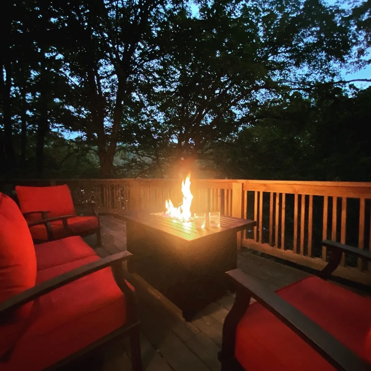 A private outdoor deck with a fire pit surrounded by red chairs, set against a backdrop of lush woods. The cozy, intimate setup is perfect for stargazing or sharing stories by the fire on peaceful evenings.