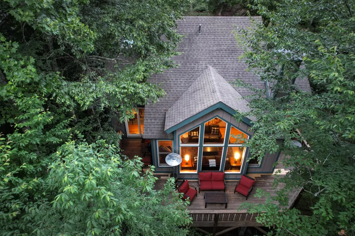 A wide deck featuring red outdoor furniture, large windows, and a view of the surrounding trees, inviting guests to relax outdoors, socialize, or enjoy quiet mornings and evenings amid nature.