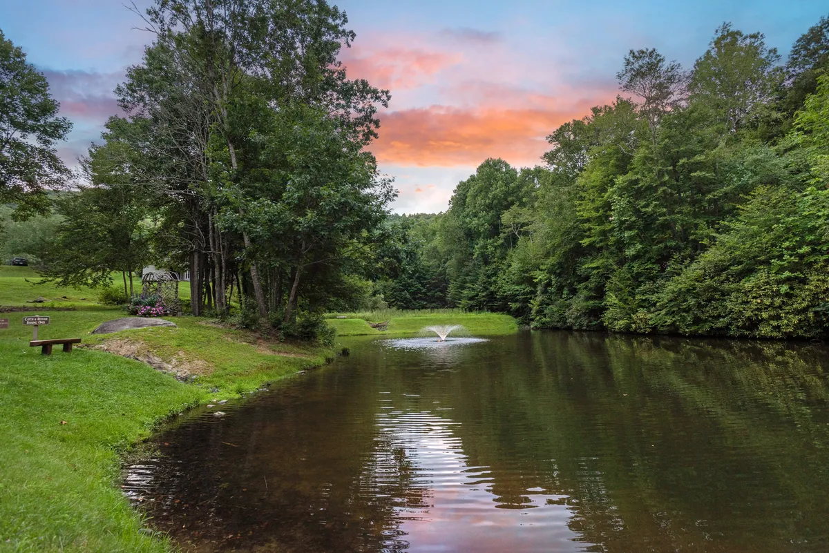 A peaceful pond with a central fountain, surrounded by lush greenery and a colorful sky reflected in the calm water. This natural amenity is ideal for fishing, picnicking, or simply enjoying tranquil moments outdoors.