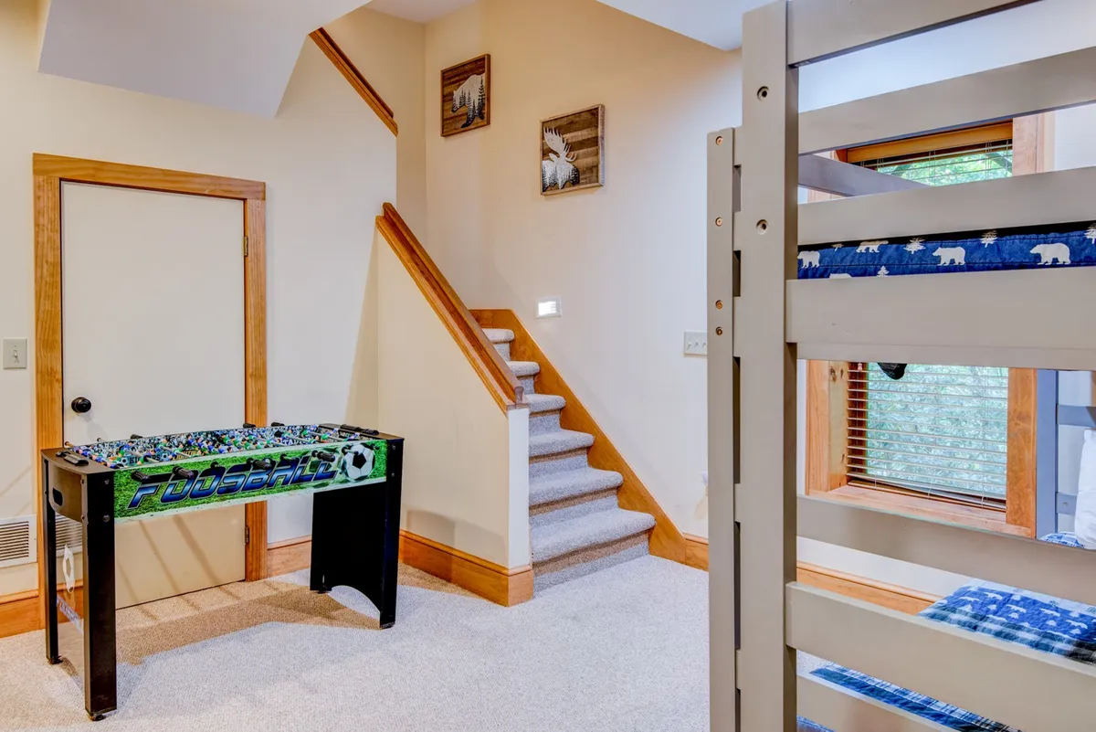 Inside, a cozy multi-level game and bunk room features a foosball table, sturdy wooden bunk beds, and cheerful decor. Large windows let in natural light and offer glimpses outside, connecting playtime with the beauty of the mountains.