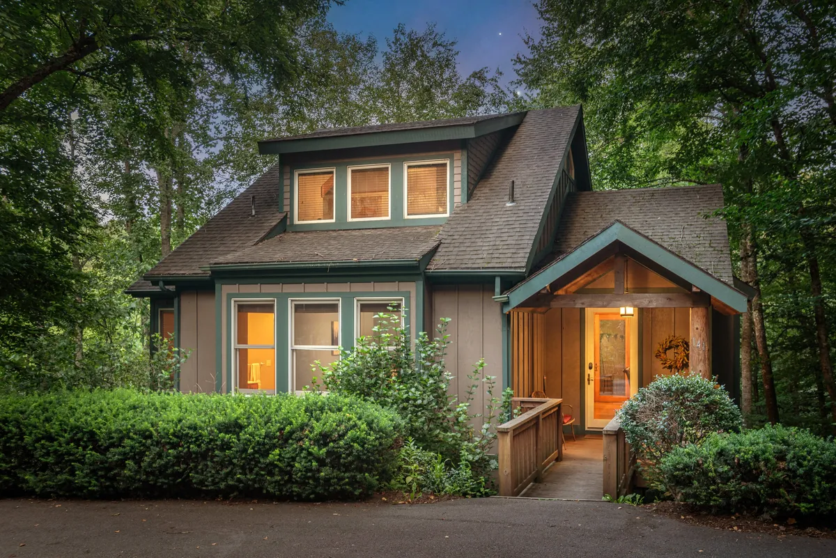 A welcoming exterior view of the front entrance, surrounded by landscaping and forest. The inviting ambiance suggests a peaceful retreat and serves as the literal and figurative threshold to outdoor exploration.